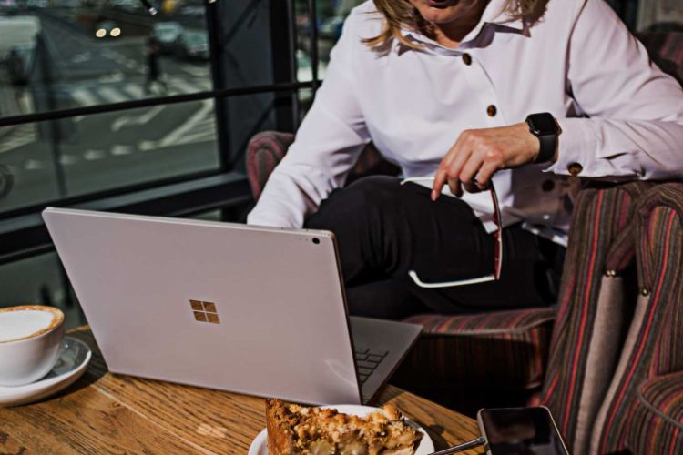 Women in a coffee shop looking at a laptop with glasses in her hand