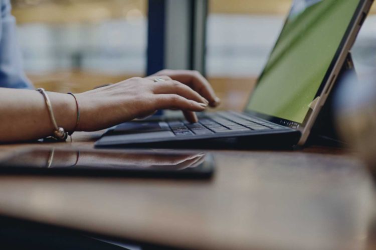 person at a desk on a laptop with a smartphone on the table