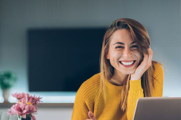 Woman in a yellow jumper on a laptop with a coffee mug in hand